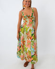Woman in floral maxi dress with colorful earrings and brown sandals smiling