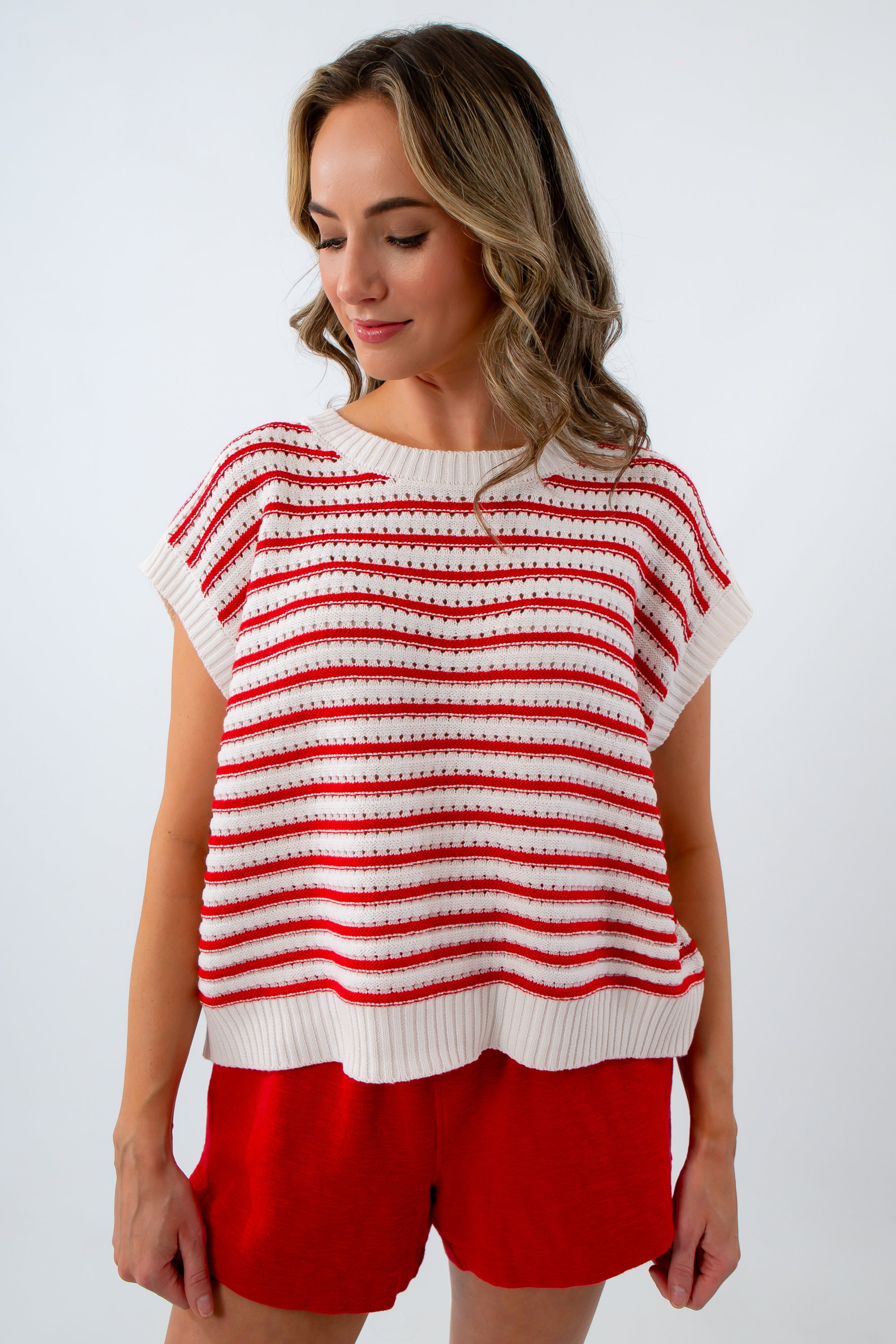 Woman wearing a red and white striped sleeveless top with red shorts on a white background