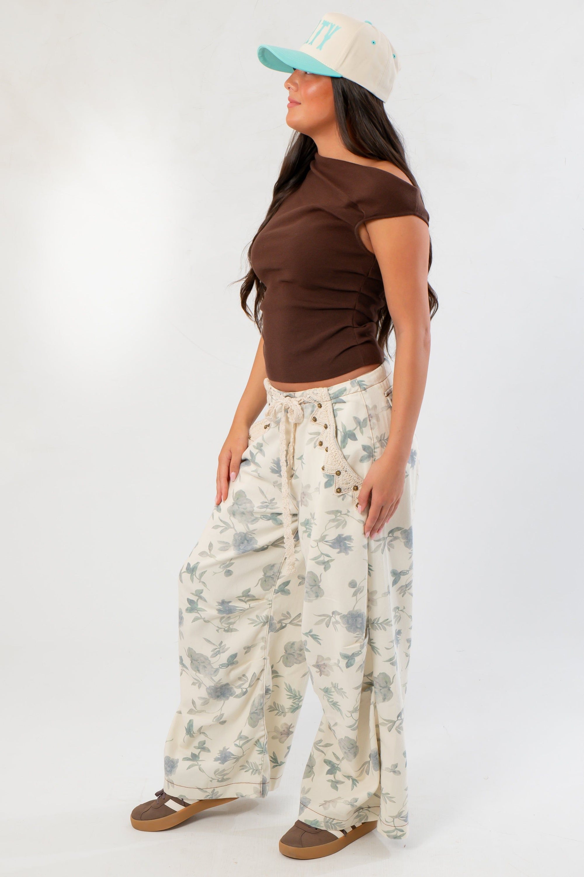 Side view of Friday Feeling Brown Asymmetrical Top styled with floral pants, highlighting the top’s flattering twist detail.