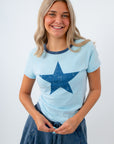 Woman wearing a light blue t-shirt with a blue star design on a white background for harry styles concert