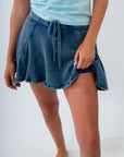 Person wearing a light blue top and denim skirt on a white background