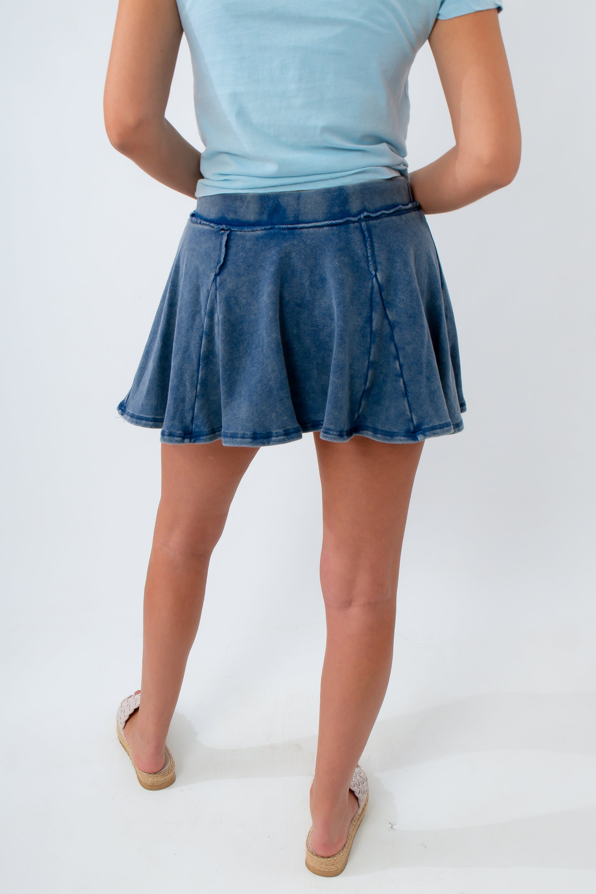 Person wearing a blue denim skirt and light blue top on a white background