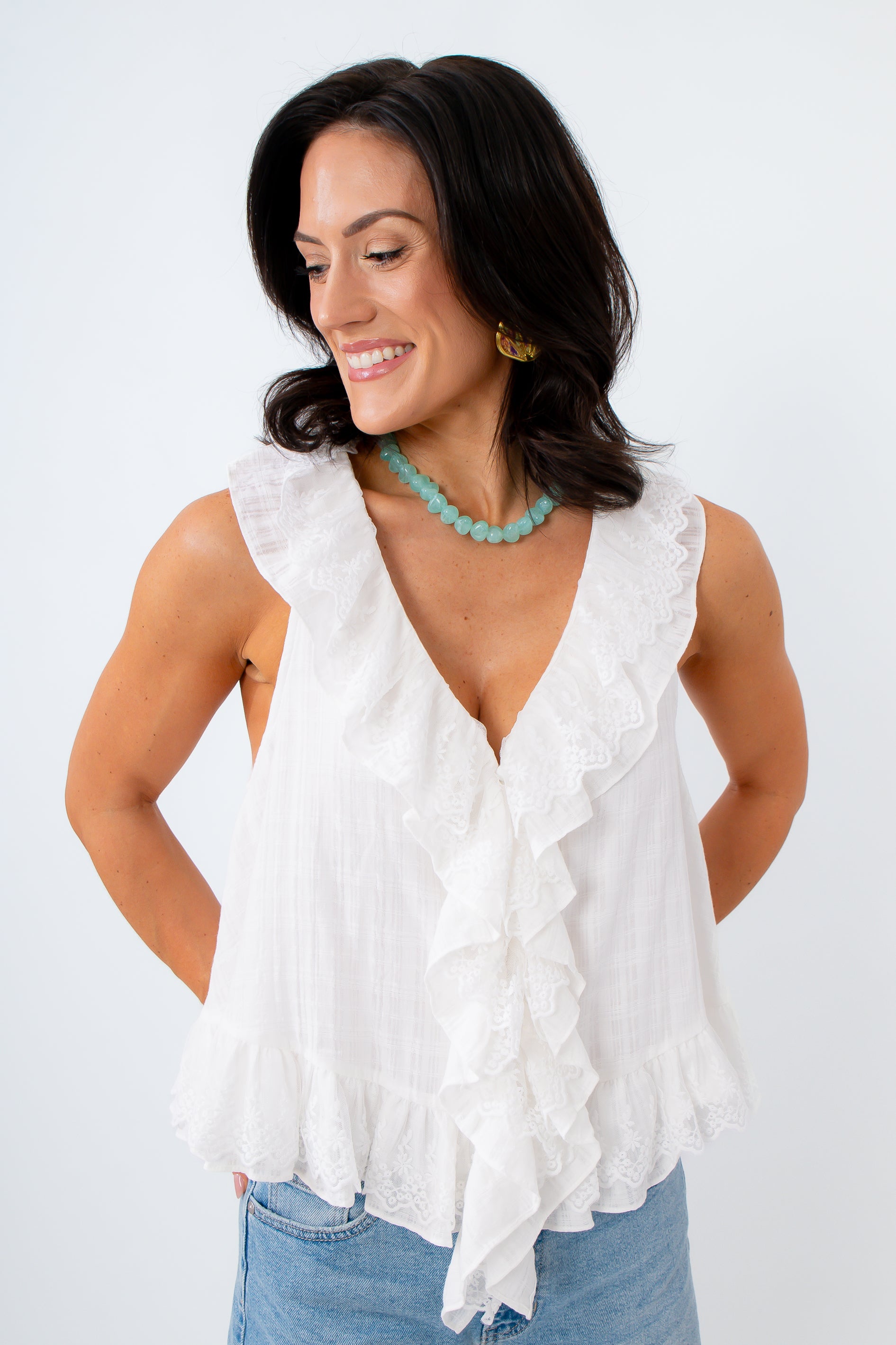 Woman wearing a white ruffled top and blue jeans against a white background