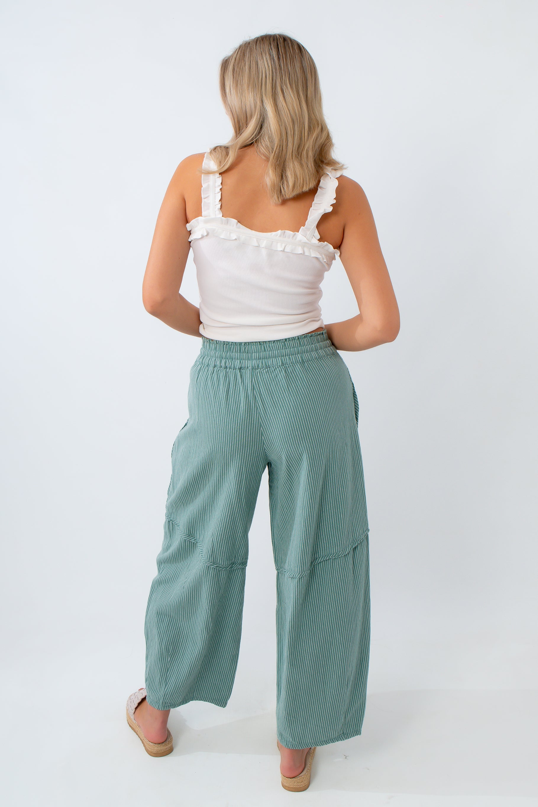 Woman wearing a white top and teal pants on a white background