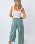 Woman wearing a white top and teal pants on a white background