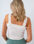 Woman wearing a white sleeveless top with ruffle details on a plain background