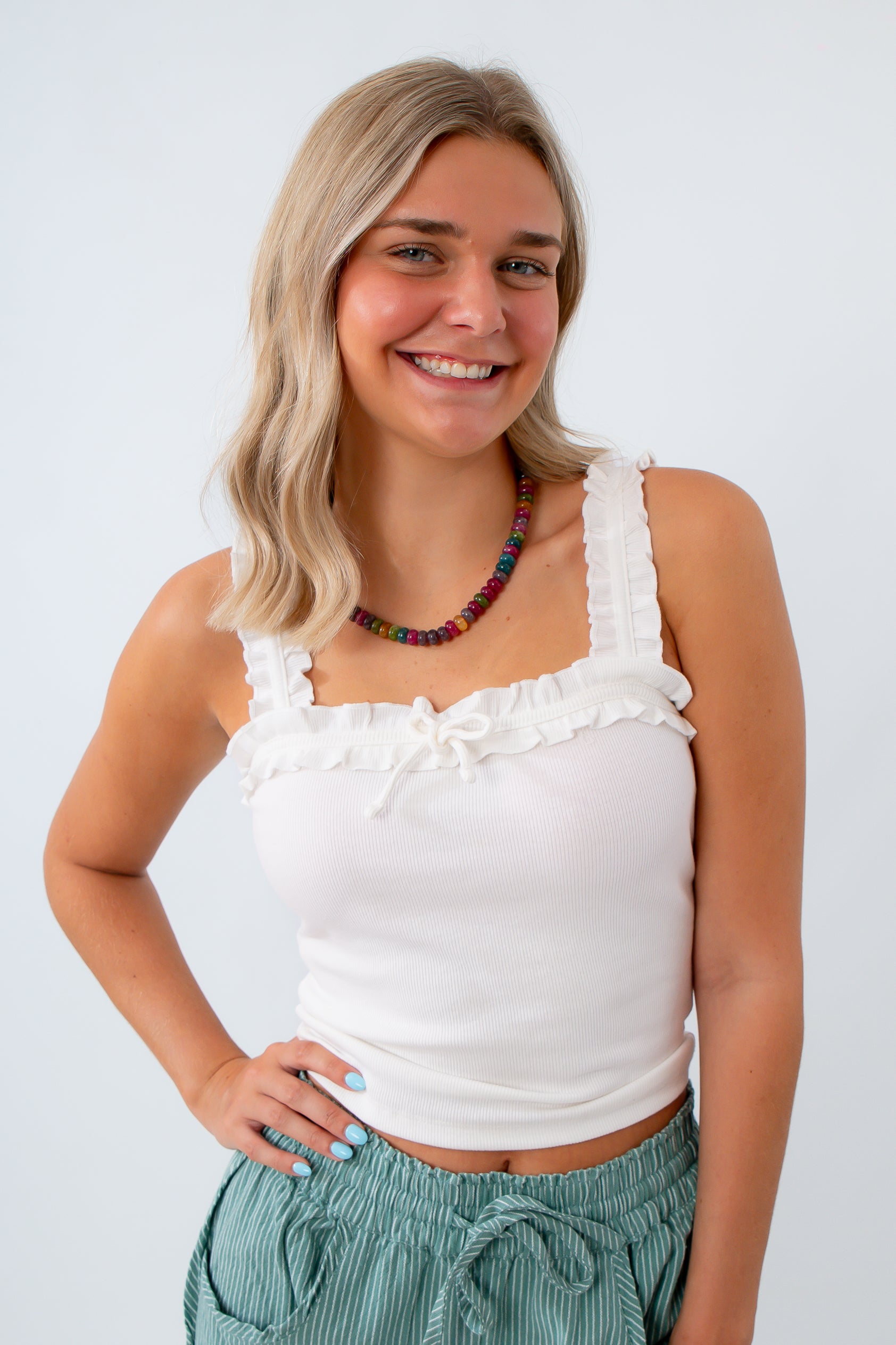 Woman wearing a white sleeveless top with ruffles and green pants on a white background