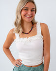 Woman wearing a white sleeveless top with ruffles and green pants on a white background