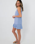 Back view of woman in blue pleated hem mini dress with sunglasses and beige slide sandals