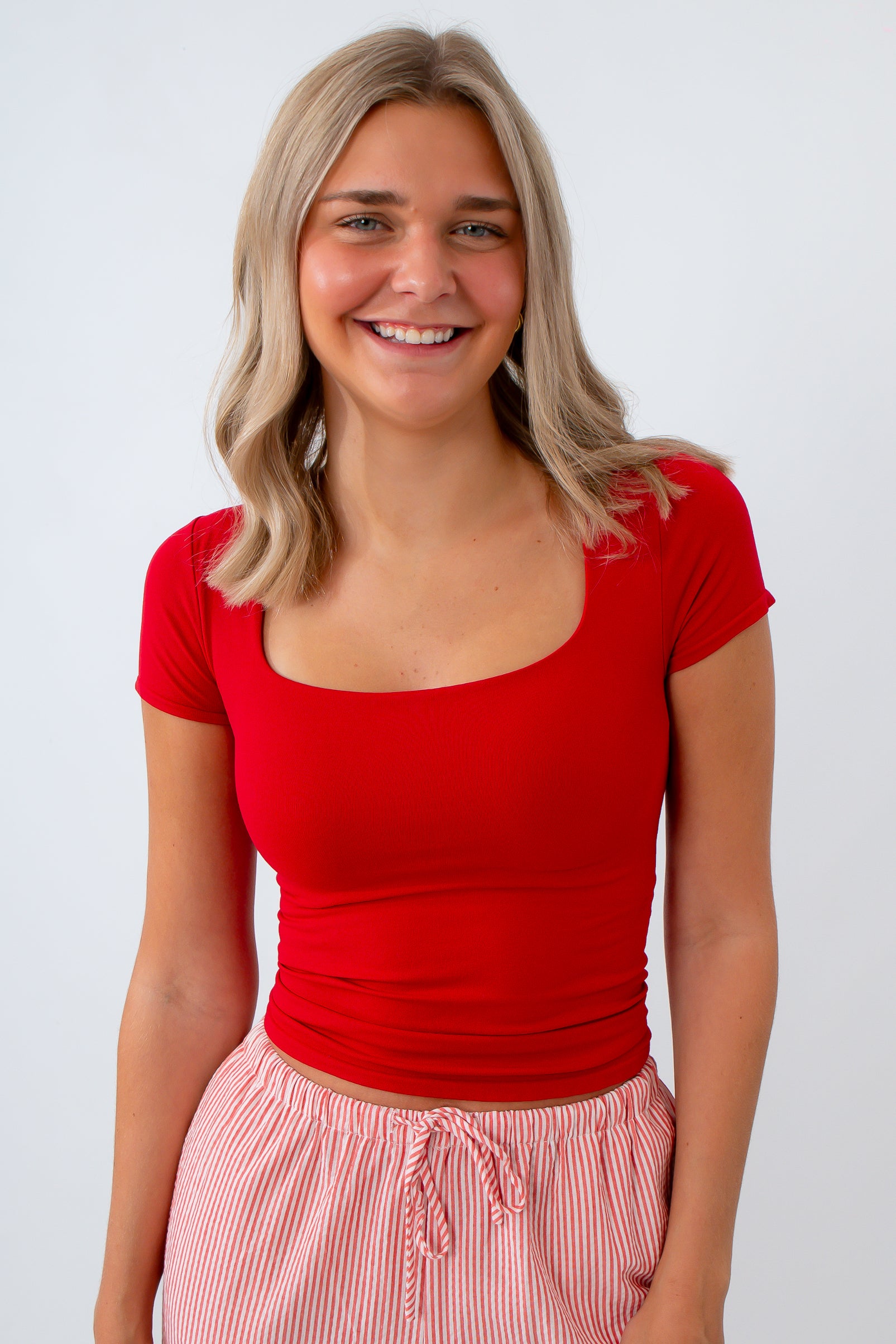 Woman wearing a red top and pink striped pants on a white background