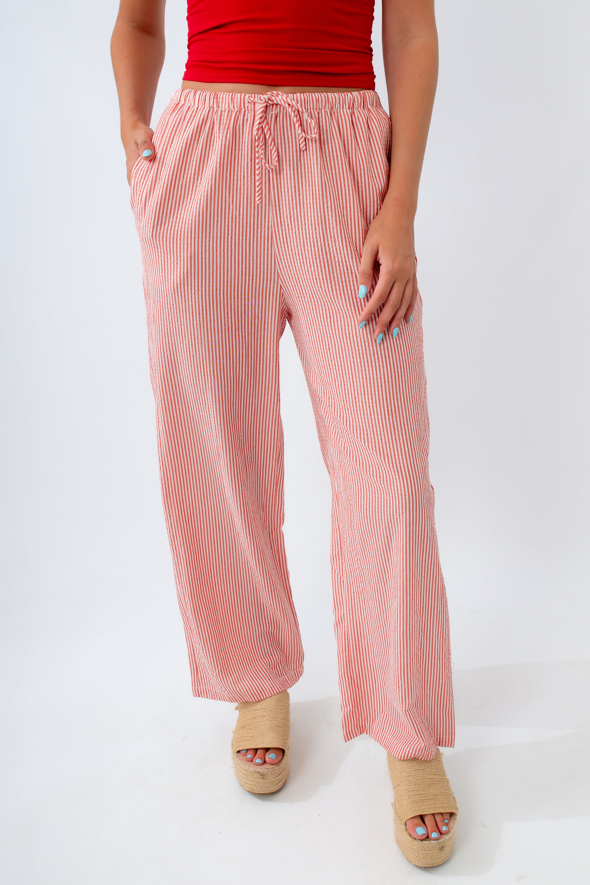 Person wearing pink striped pants and a red top on a white background
