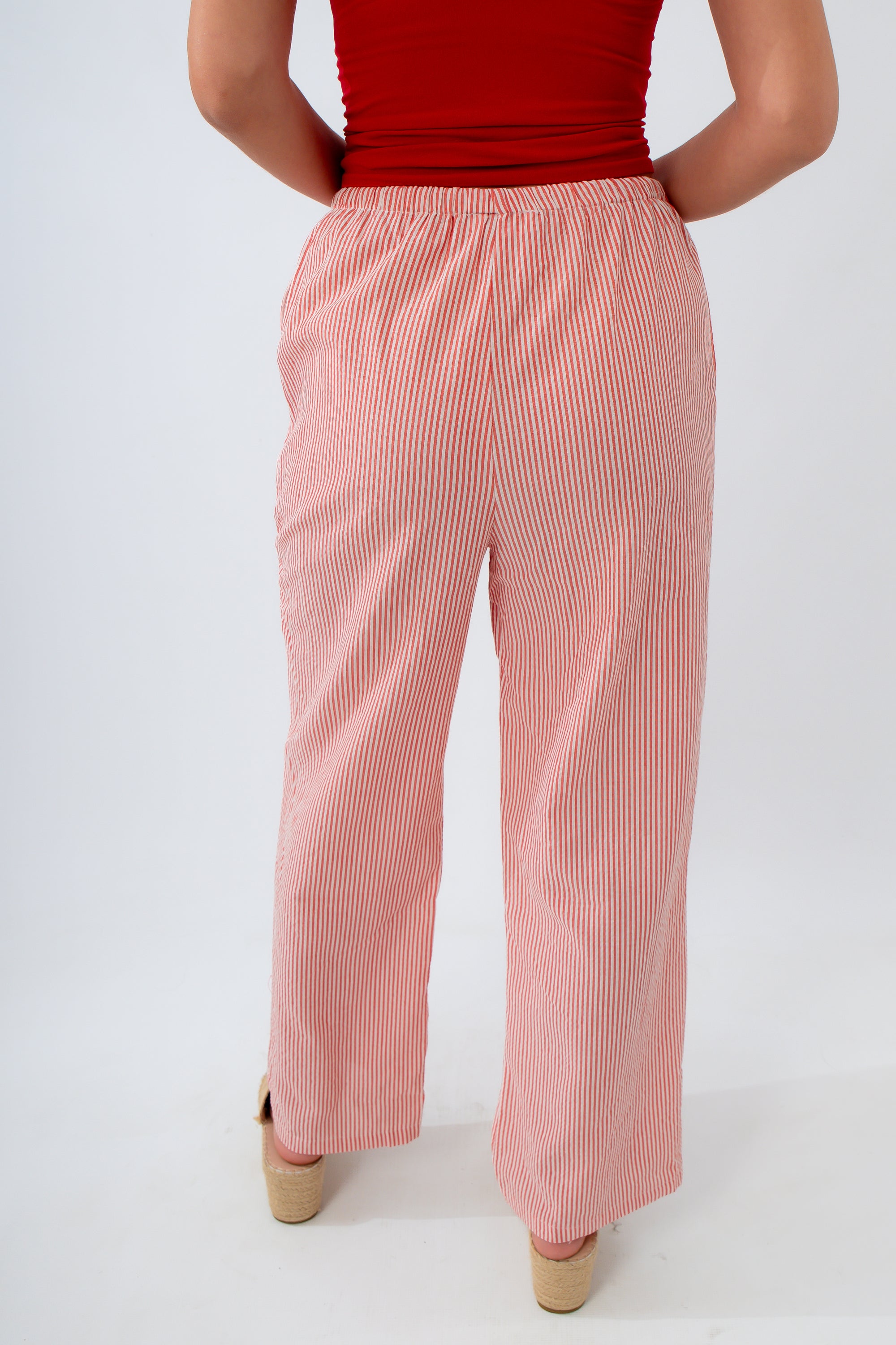 Person wearing a red top and pink striped pants on a white background