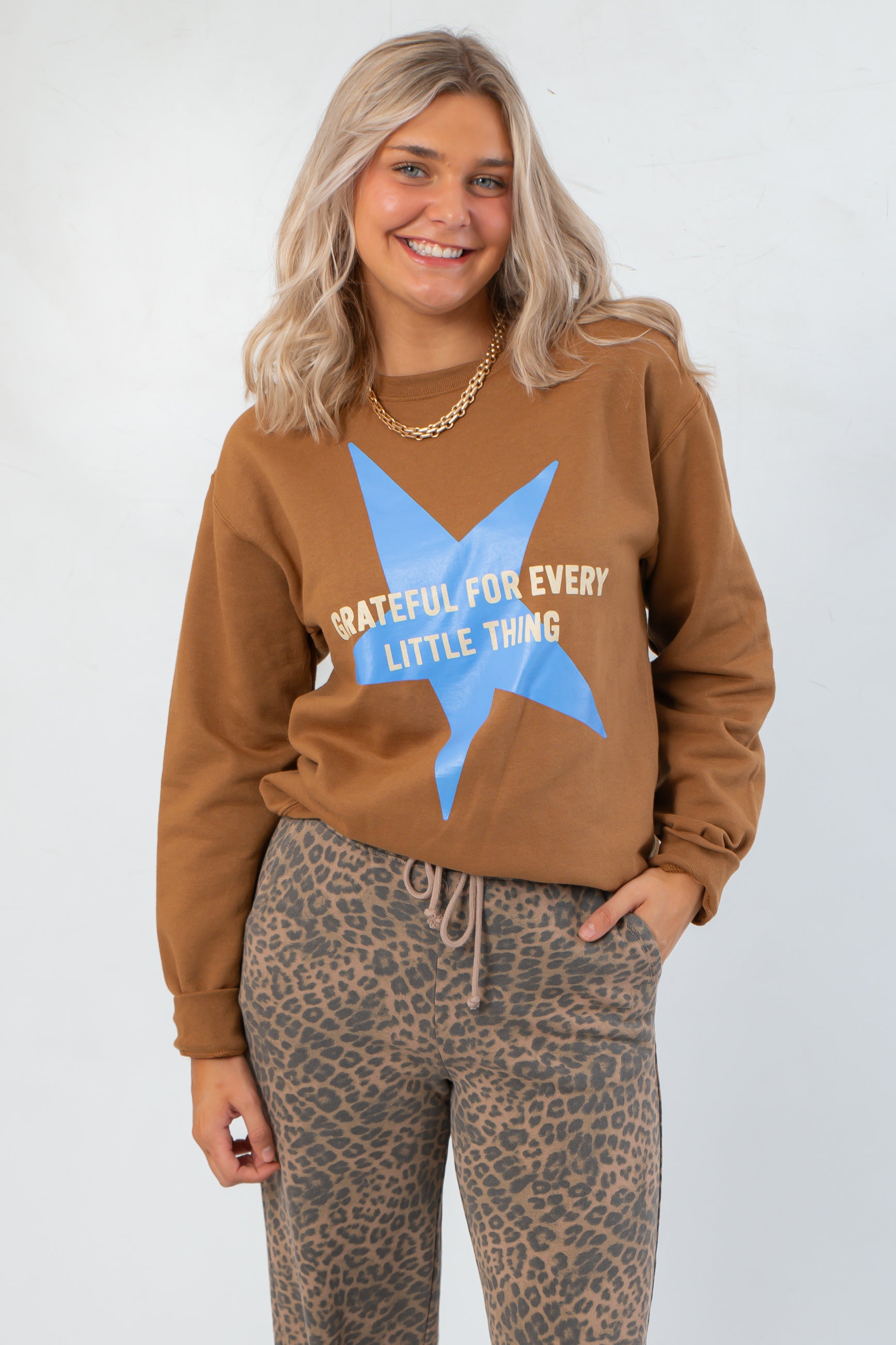 Grateful for Everything Graphic Star Sweatshirt in brown with blue star and white text, styled with leopard print pants. Cozy fall knit top.
