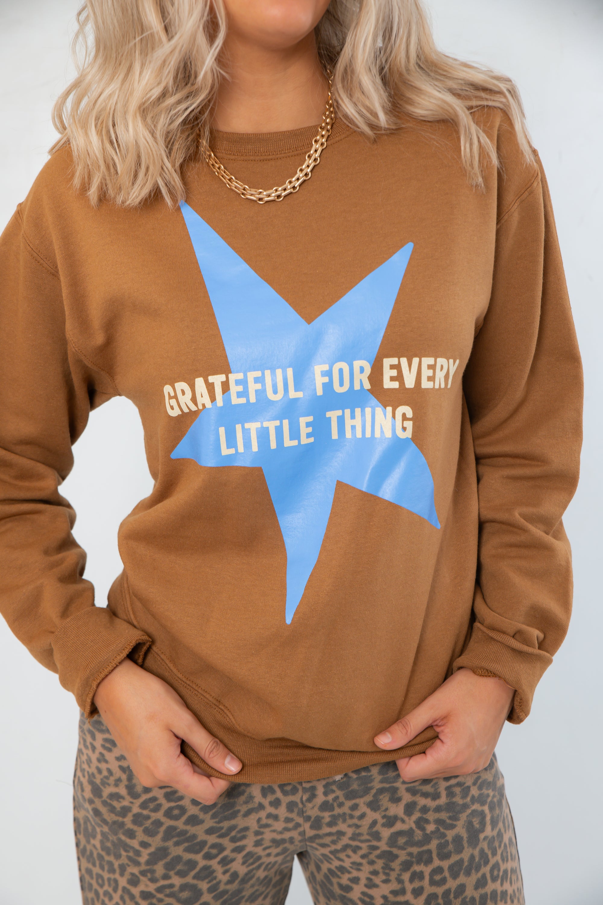 Close-up of Grateful for Everything Graphic Star Sweatshirt showing blue star graphic and white text on soft brown fabric. Ideal for cozy fall looks.