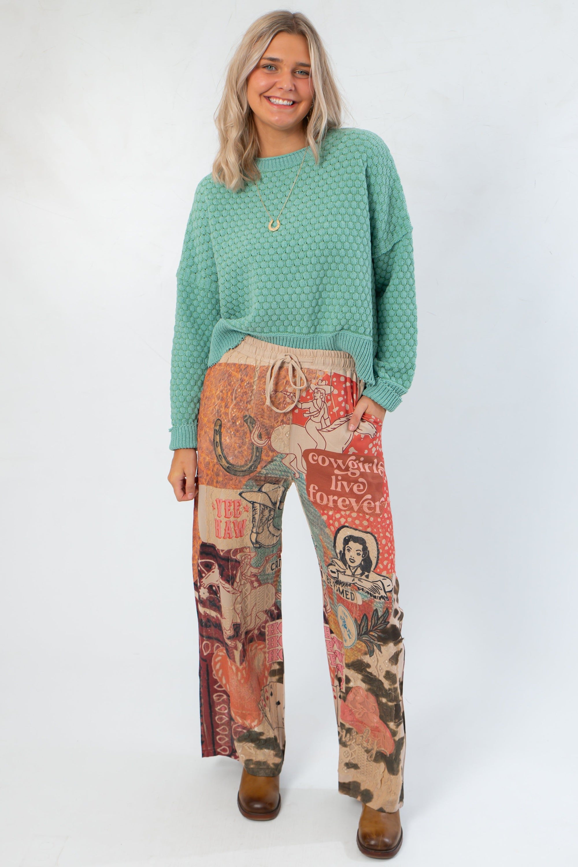 Model wearing Ori Howdy Drawstring Pants with turquoise sweater, showcasing western-themed pattern and comfortable fit.