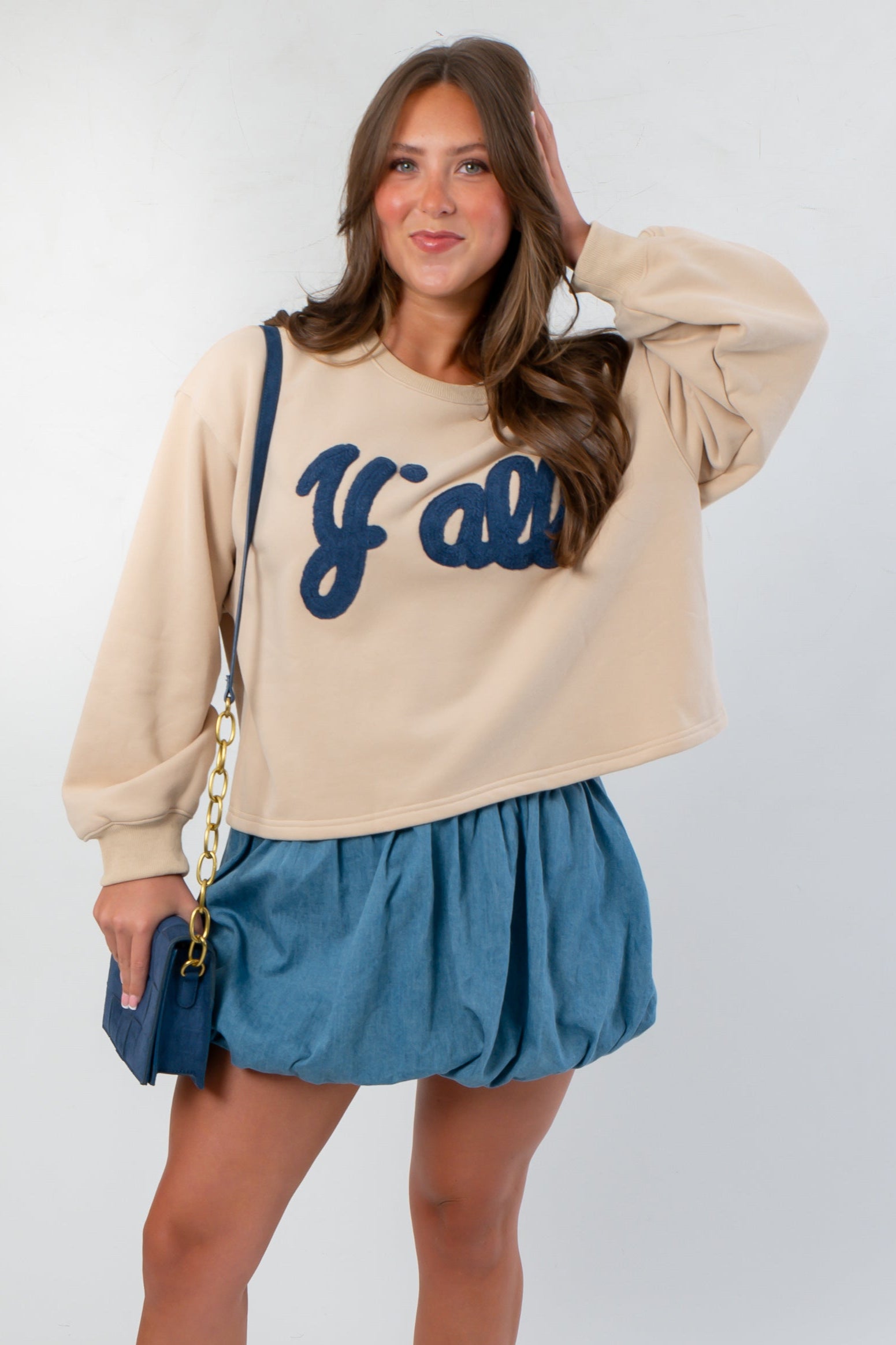 Southern Chic “Y’all” Flocked Sweatshirt in beige with bold navy flocked lettering, styled with a denim skirt for a trendy Western-inspired look.