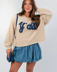 Southern Chic “Y’all” Flocked Sweatshirt in beige with bold navy flocked lettering, styled with a denim skirt for a trendy Western-inspired look.