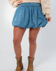 Close-up of Denim Bubble Skort - Mini Skort with high waist and gathered bubble hem, paired with tan boots for a casual outfit.
