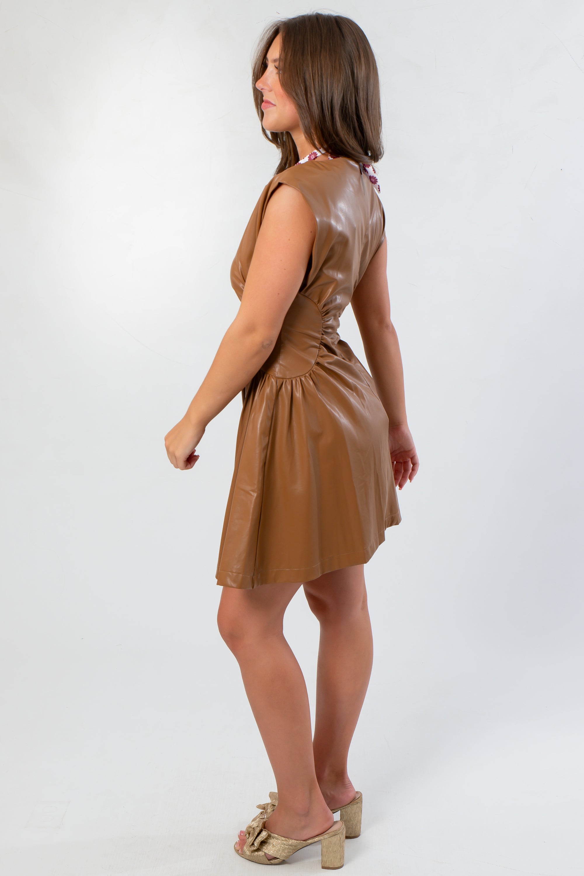 Side profile of Coffee Date Chocolate Faux Leather Mini Dress showing ruched waist detail and smooth faux leather texture.