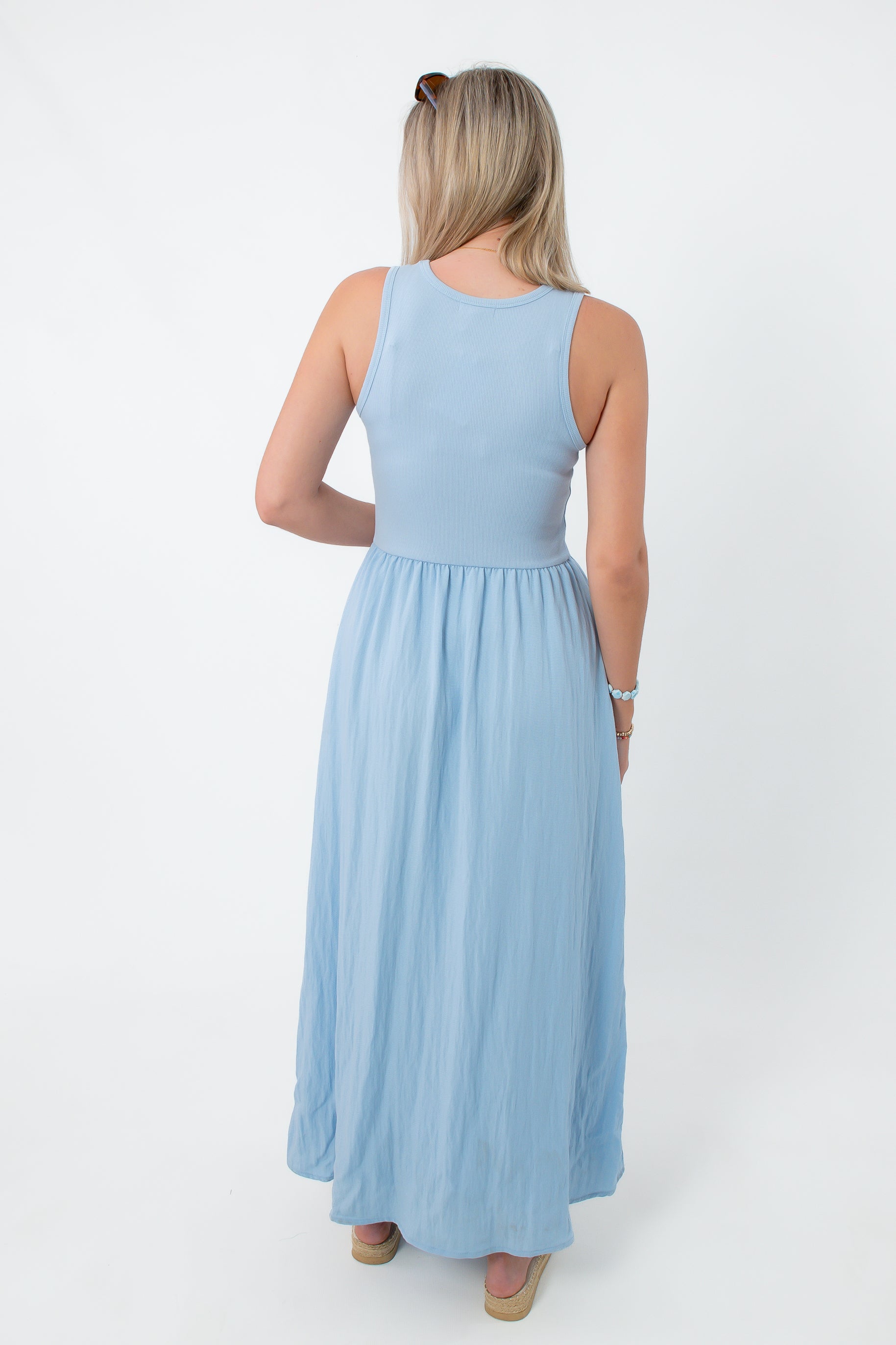 Front view of woman in light blue sleeveless maxi dress, holding a beach tote bag