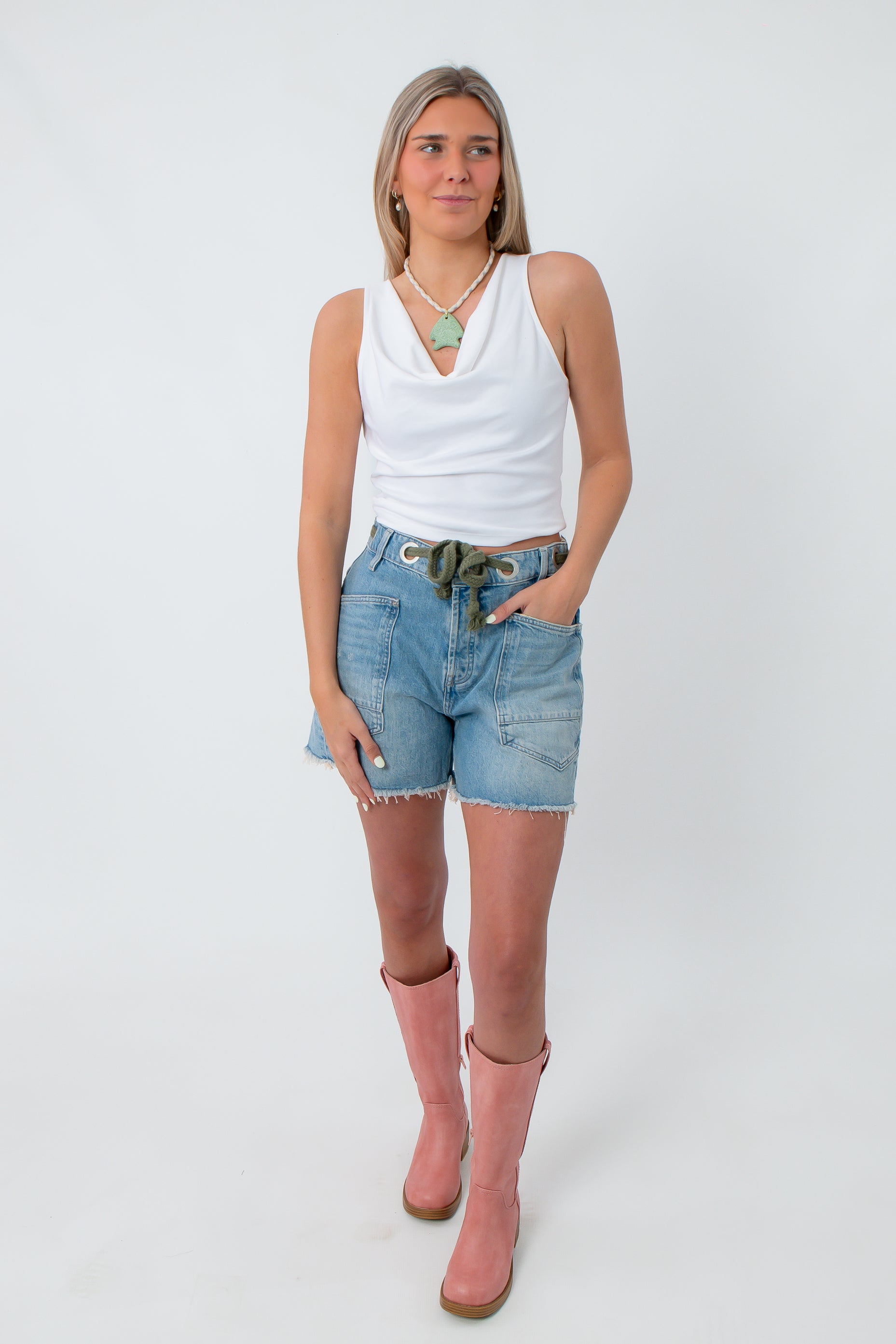 White sleeveless cowl neck top with draped neckline, styled with denim shorts and pink boots