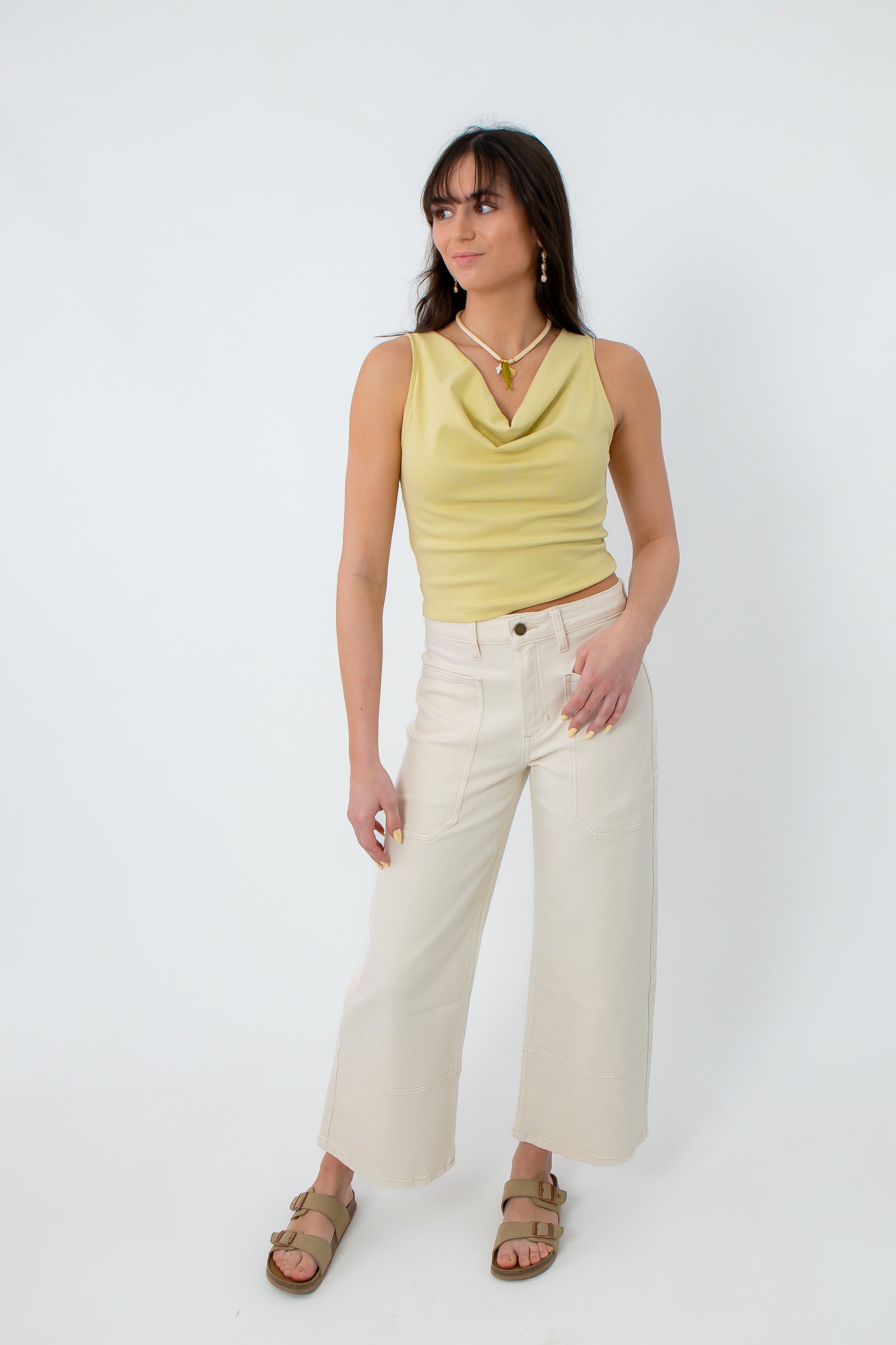 Close-up of model in yellow sleeveless cowl neck top with jewelry