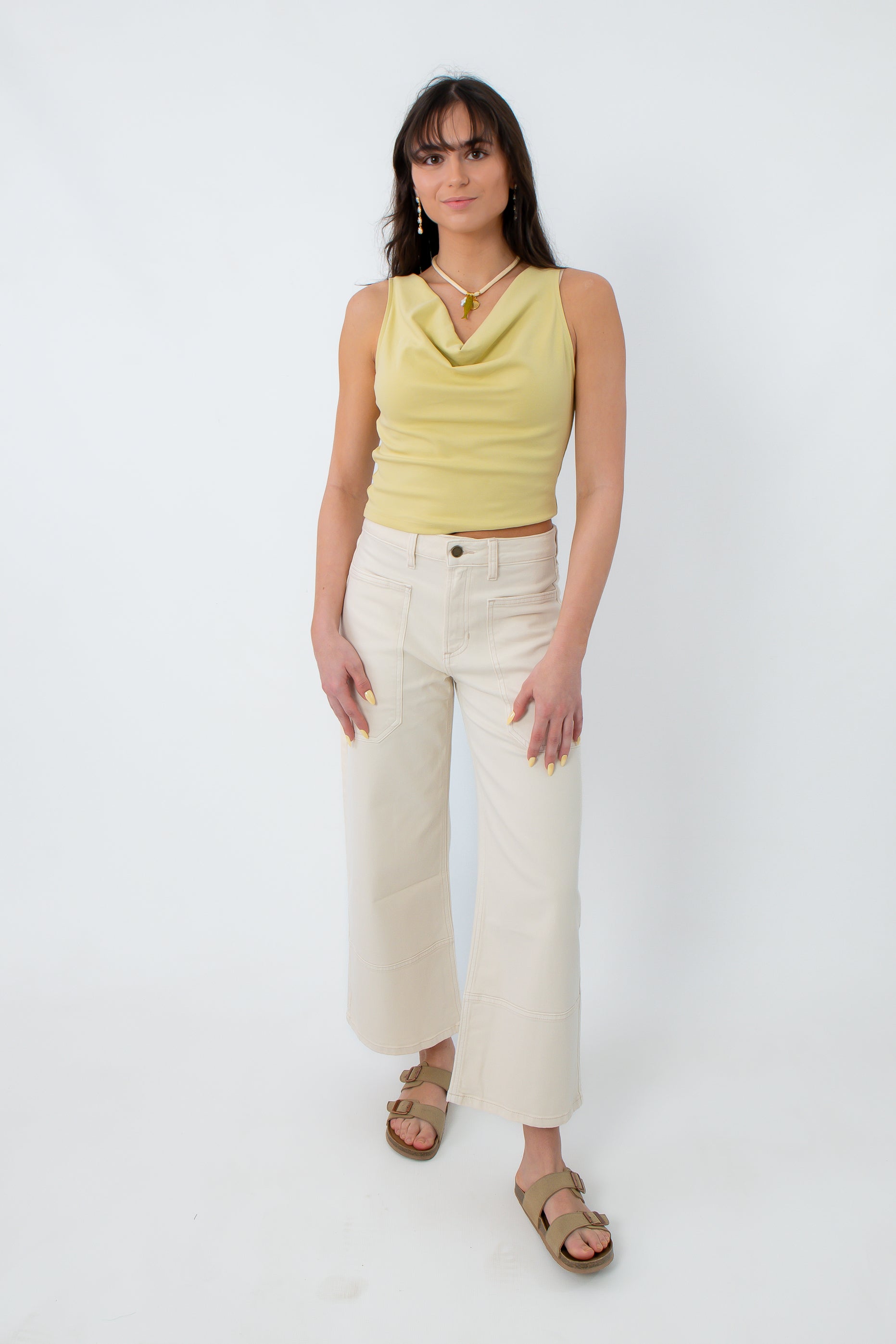Model wearing yellow sleeveless cowl neck top with cream wide-leg pants and sandals