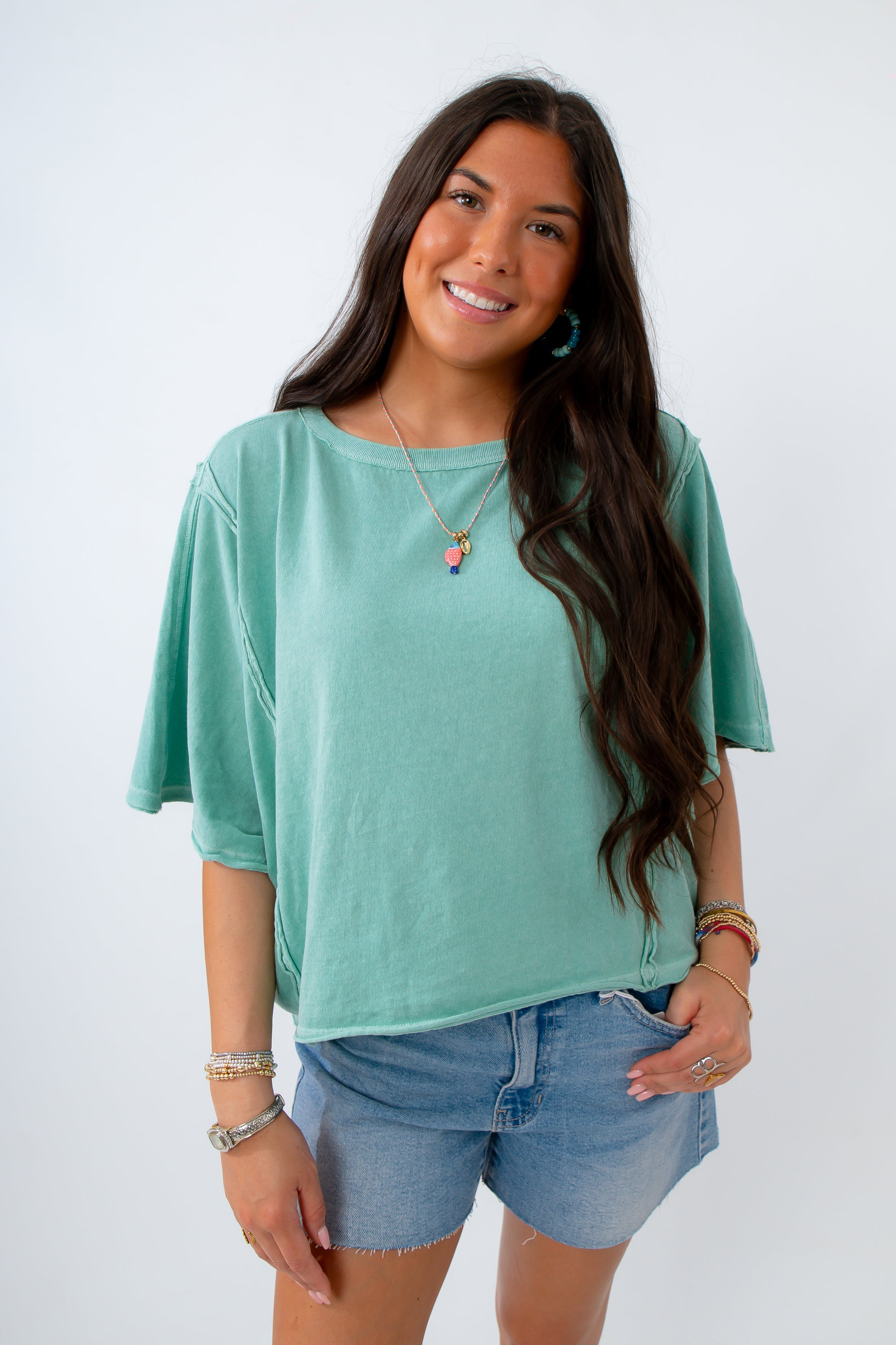 Woman wearing a light green top and denim shorts against a white background
