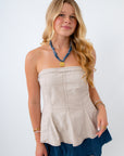 Woman wearing a beige strapless top and blue shorts on a white background