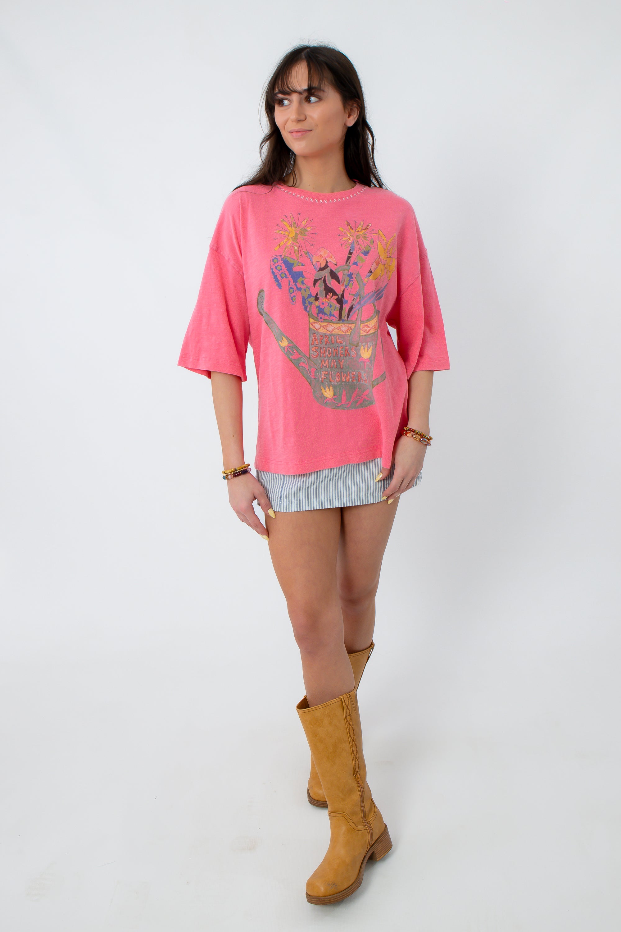 Model in pink graphic boho T-shirt with floral design, striped mini skirt, tan boots