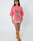 Model in pink graphic boho T-shirt with floral design, striped mini skirt, tan boots