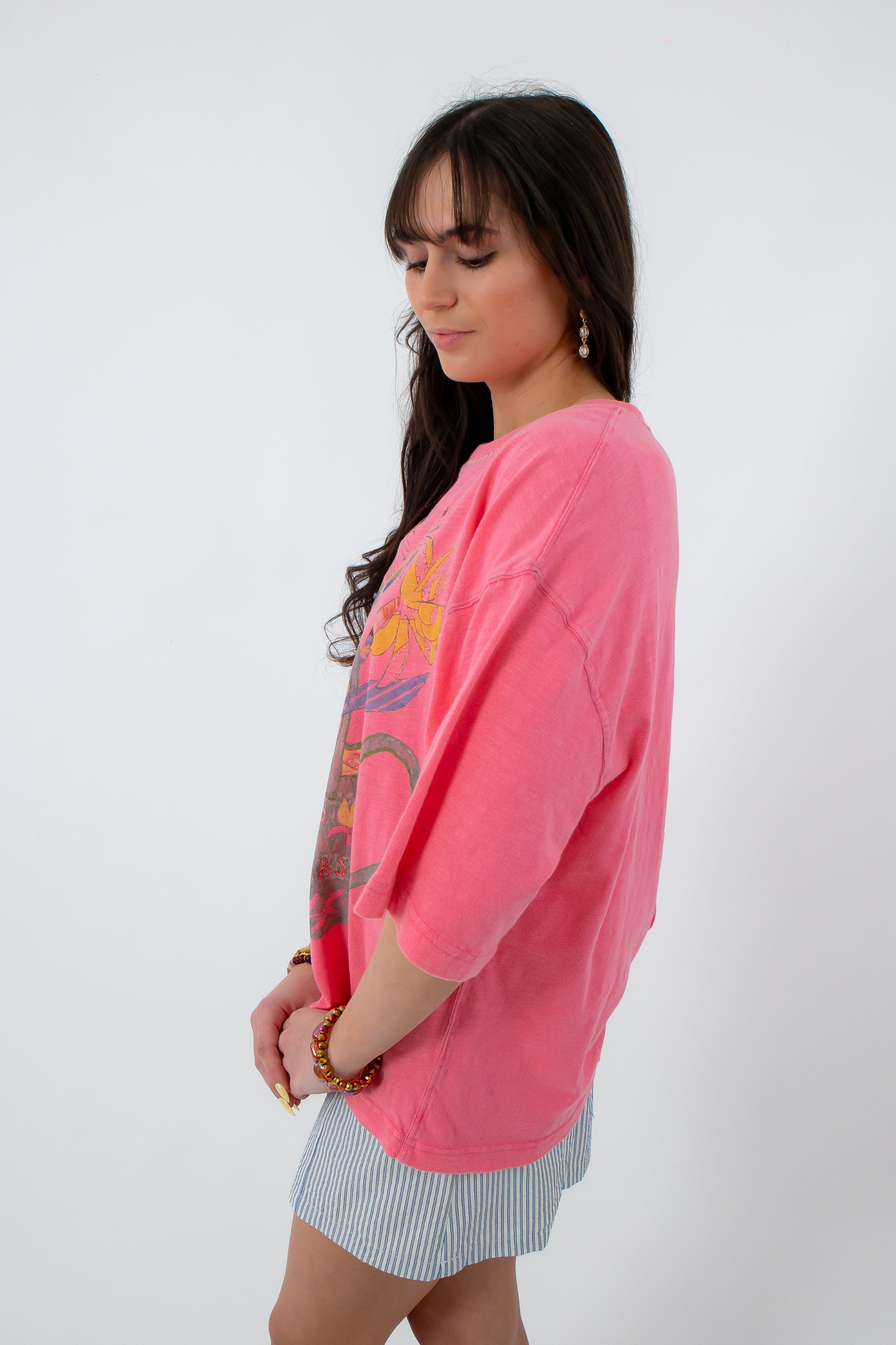 Side view of woman in pink graphic boho T-shirt, striped mini skirt, tan boots