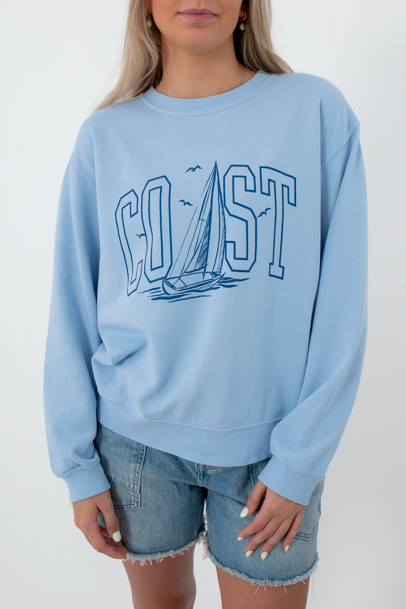 Close-up of light blue sweatshirt with 'Coast' sailboat graphic, relaxed fit women's top
