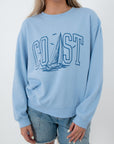 Close-up of light blue sweatshirt with 'Coast' sailboat graphic, relaxed fit women's top