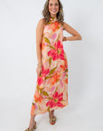 Vibrant floral maxi dress worn by smiling woman, sleeveless, colorful large flower print, perfect for wedding guests