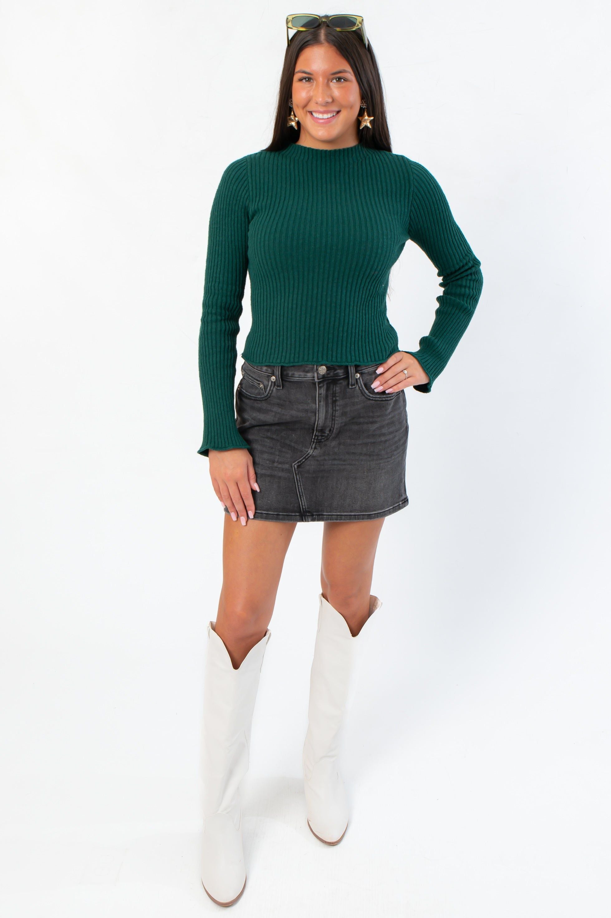 Stylish A-line Daze Spade Malibu Mid Waist Mini Skirt in dark denim, paired with a green ribbed sweater and white western boots.