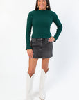 Stylish A-line Daze Spade Malibu Mid Waist Mini Skirt in dark denim, paired with a green ribbed sweater and white western boots.