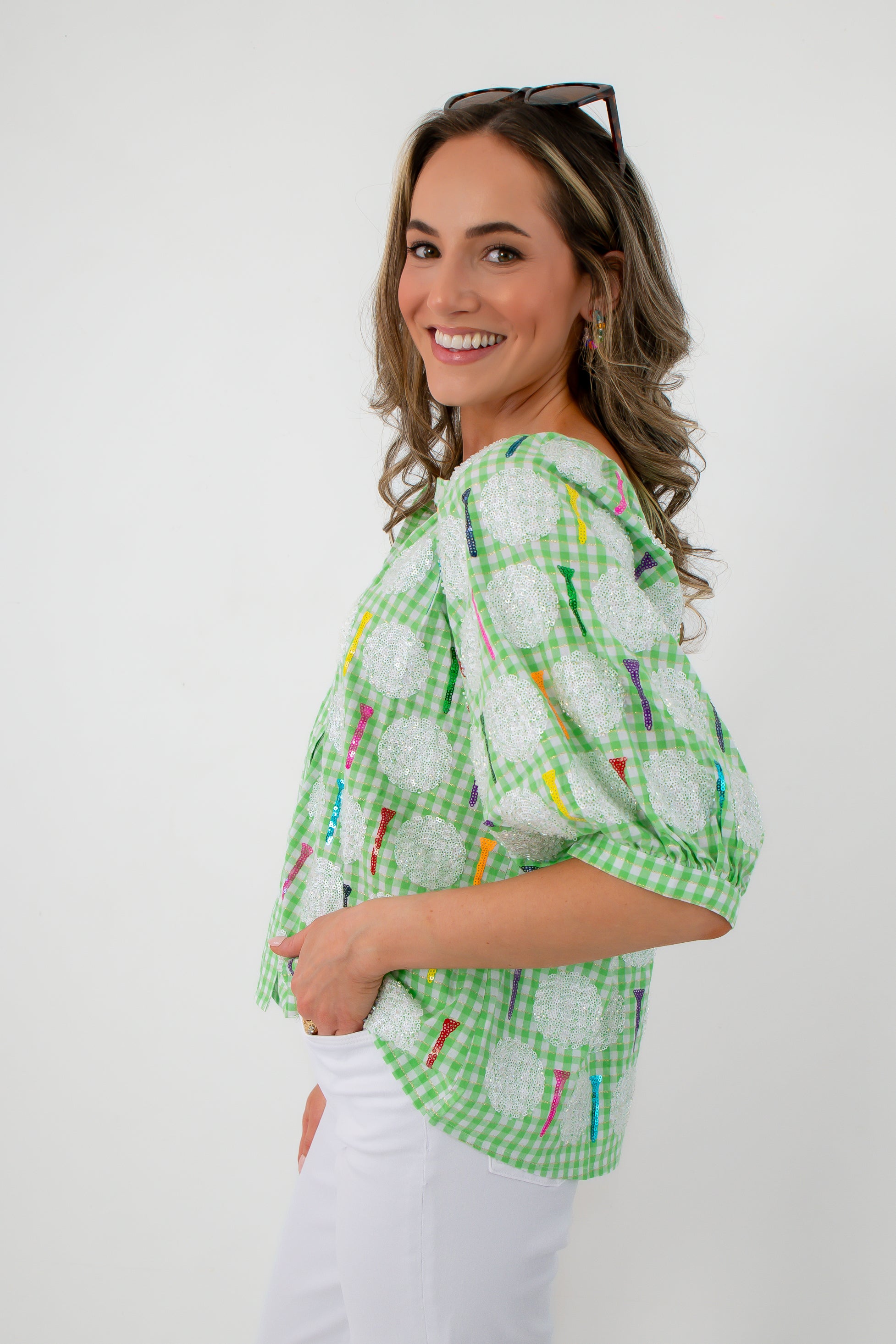 Side profile of women wearing green gingham sequin golf tee blouse with white pants