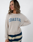 Side view of woman in beige Coastal sweater with blue text, striped skirt, sunglasses on head