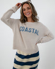 Women wearing beige Coastal sweater with blue text, striped skirt, sunglasses, smiling