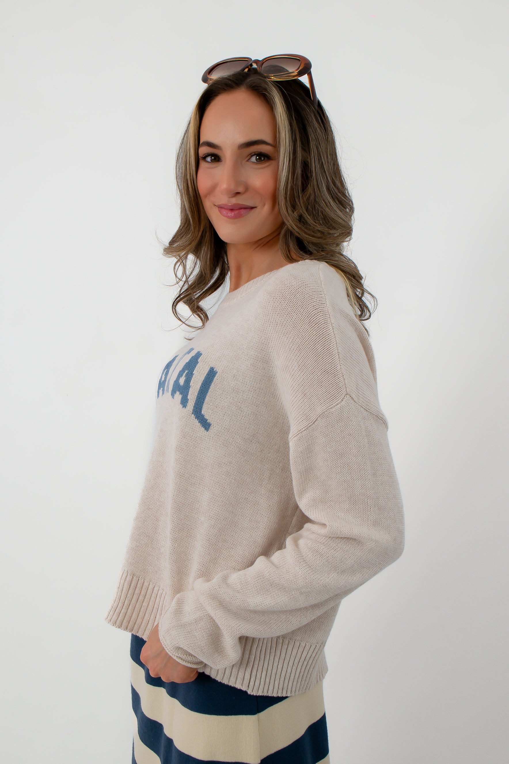 Back view of woman in beige Coastal sweater, striped skirt, sunglasses on head