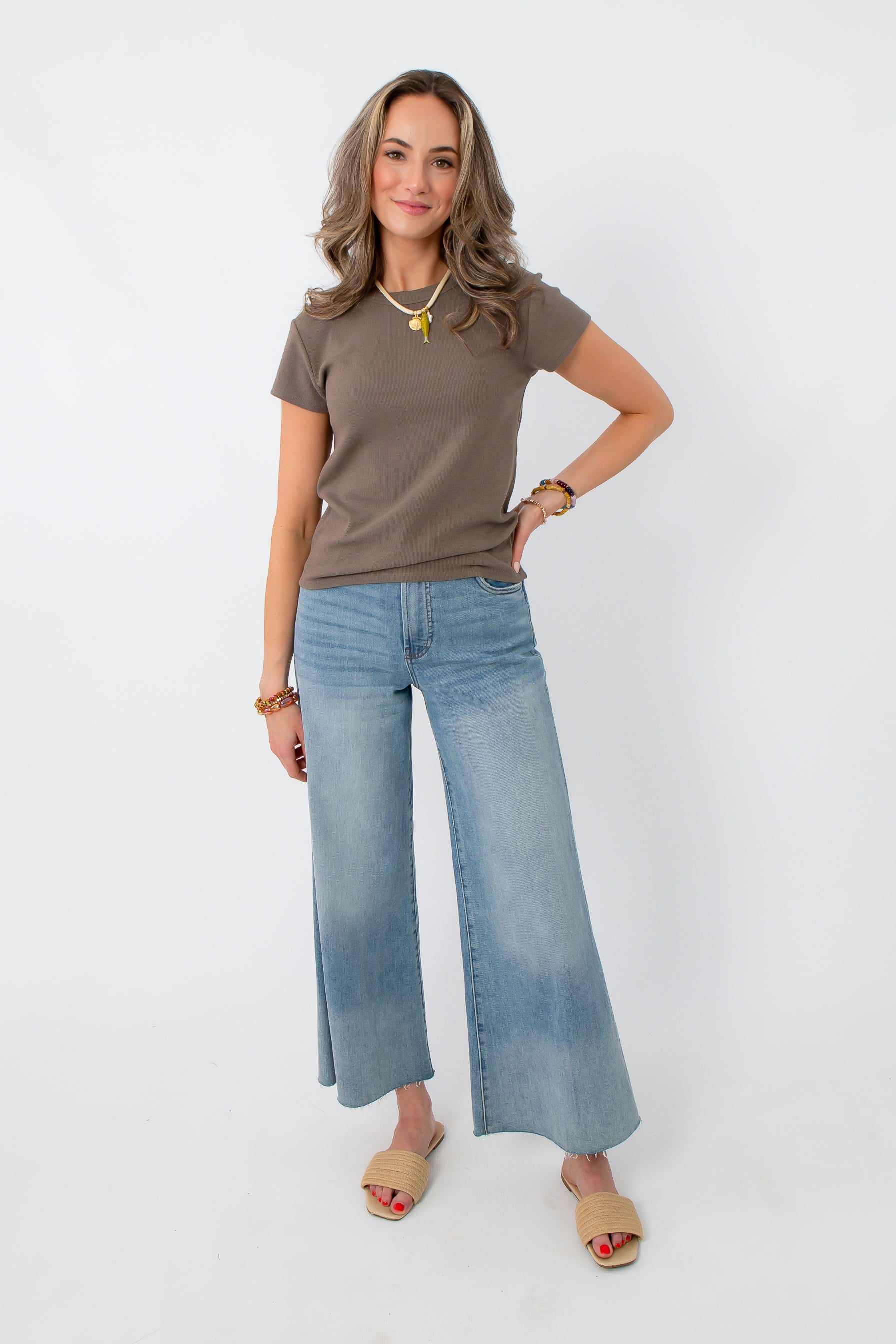Side view of woman in taupe ribbed short sleeve top, casual denim, styled with jewelry, studio background