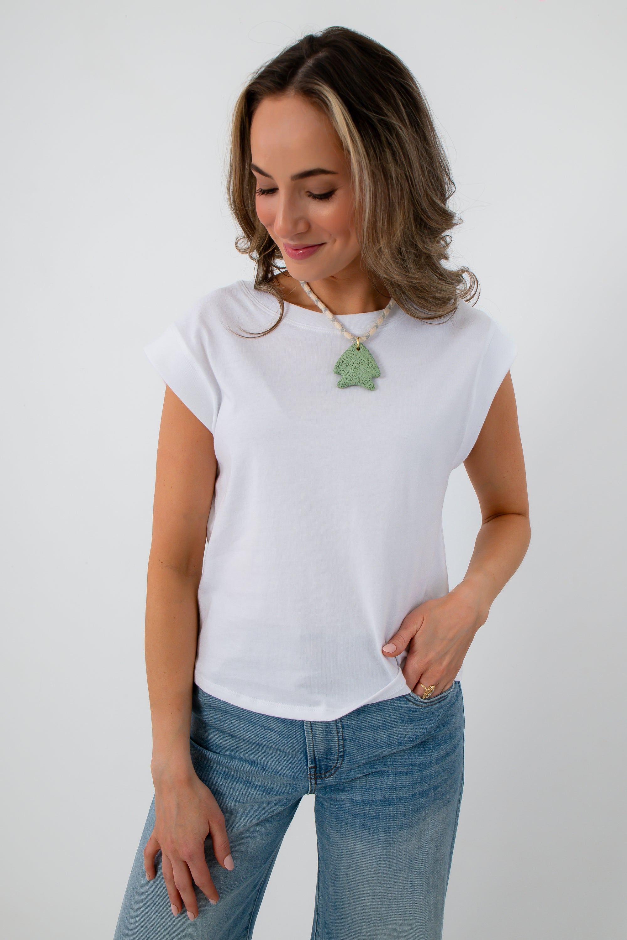 Close-up of white sleeveless Jersey top with model wearing green tree necklace