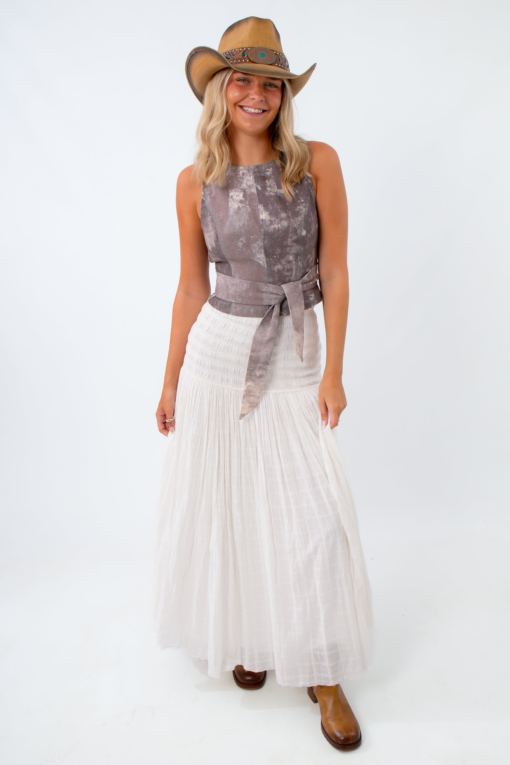 Woman wearing a sleeveless top and white skirt with a cowboy hat on a white background