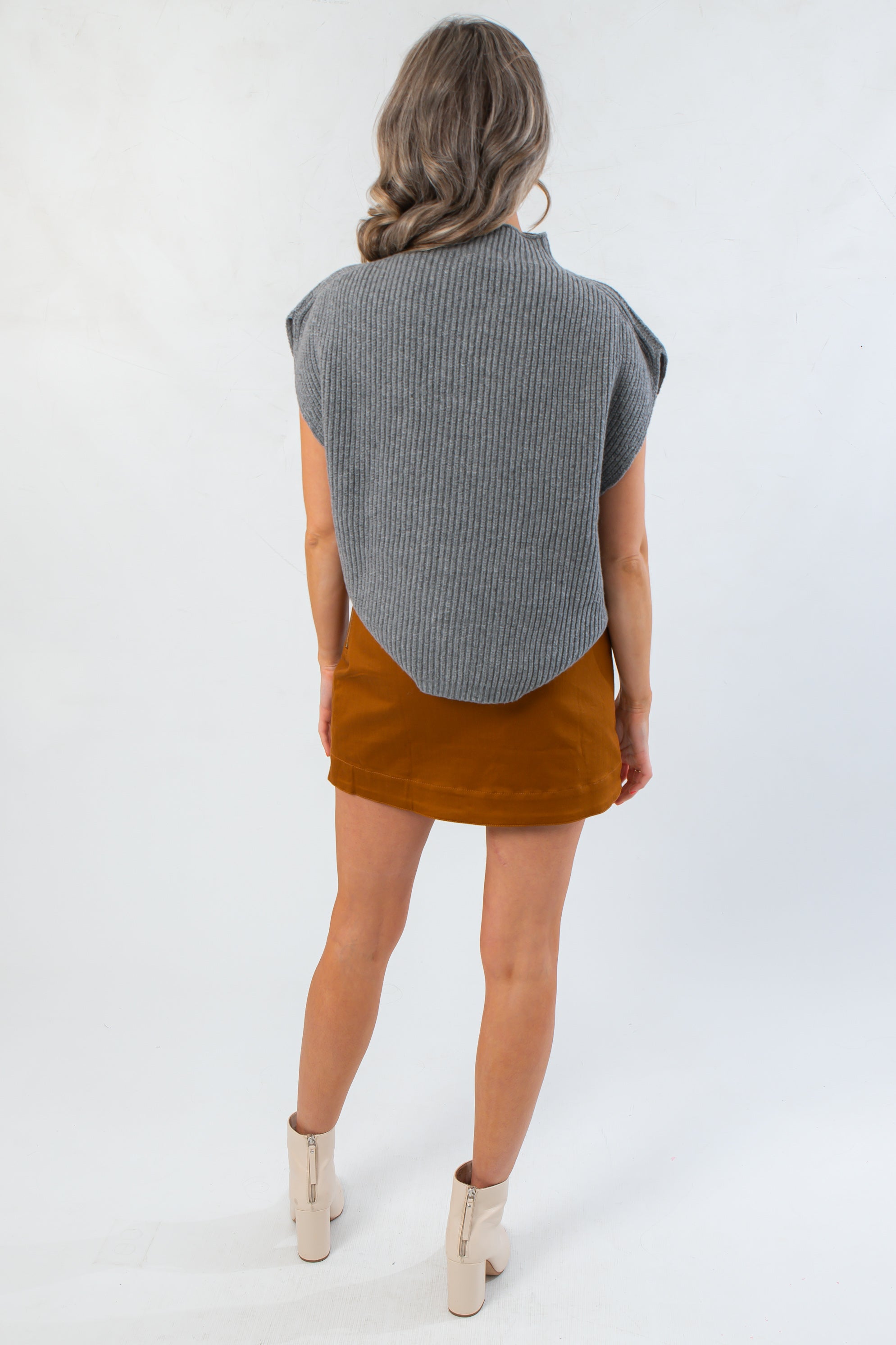Woman wearing a gray sleeveless sweater over a brown skirt on a white background
