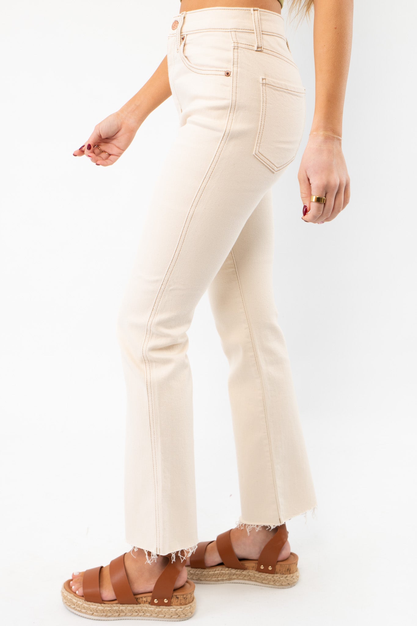 Side view of Daze Oat Milk Soho Raw Cut High Rise Ankle Flare jeans, showcasing the sleek fit, raw hem, and high-waisted silhouette in soft beige denim.