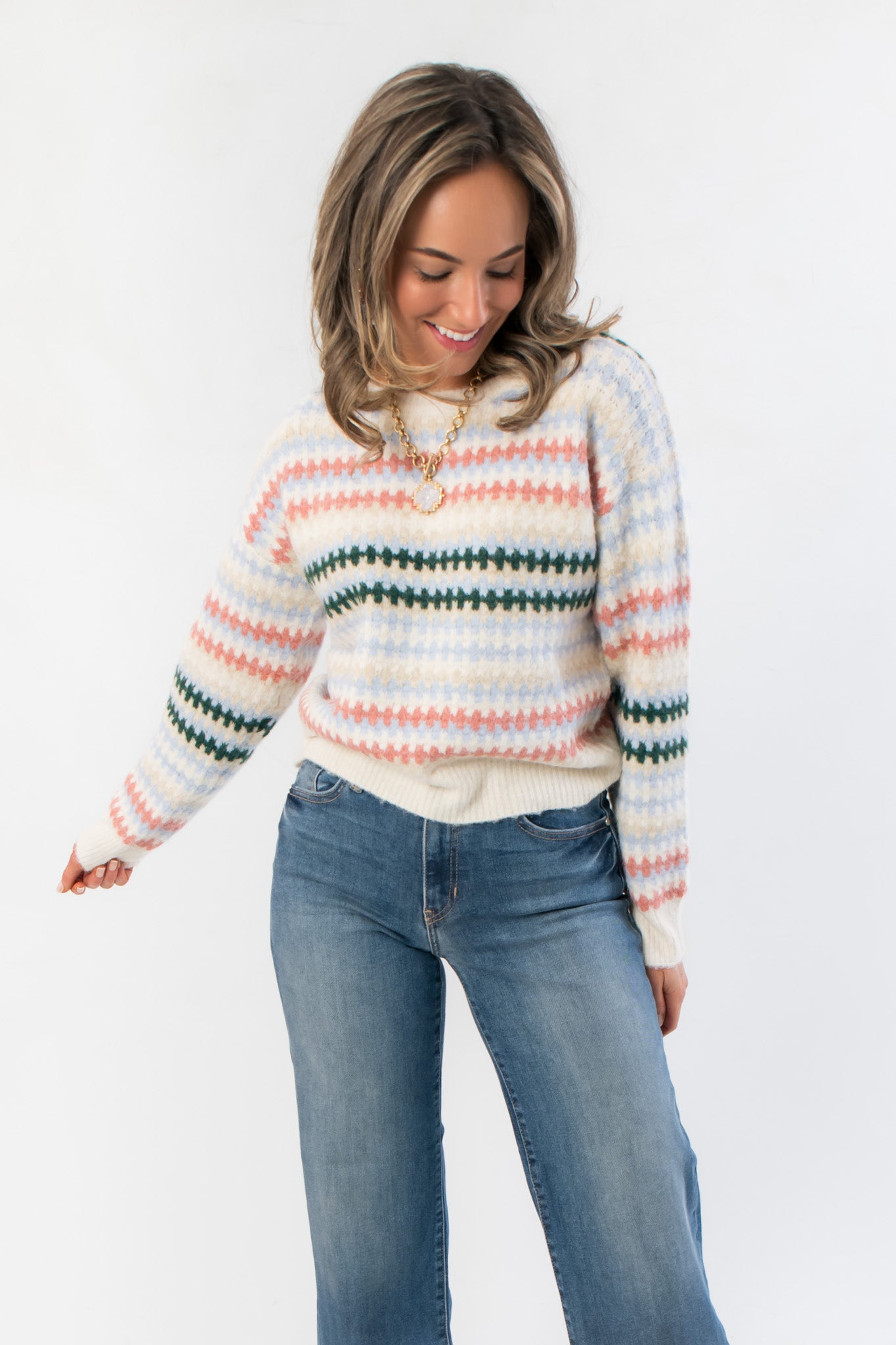 Mountain Top Stripe Knit Sweater with cozy multi color pink, blue, and green stripes, crew neck, and long sleeves styled with denim jeans.