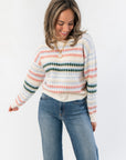 Mountain Top Stripe Knit Sweater with cozy multi color pink, blue, and green stripes, crew neck, and long sleeves styled with denim jeans.