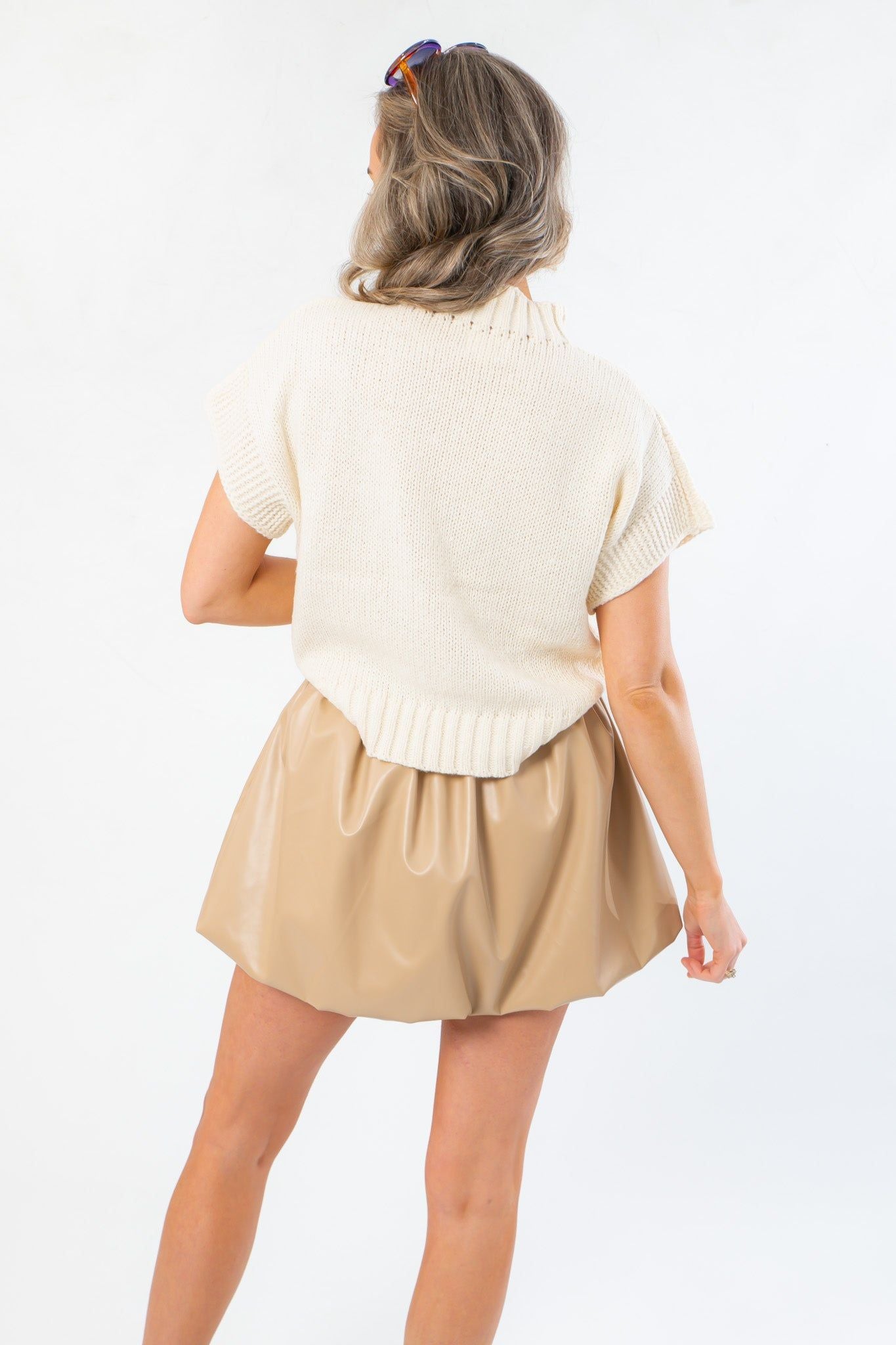 Back view of Football Bow Mock Neck Cream Sweater with ribbed hem and mock neckline, styled with a tan mini skirt for gameday fashion.