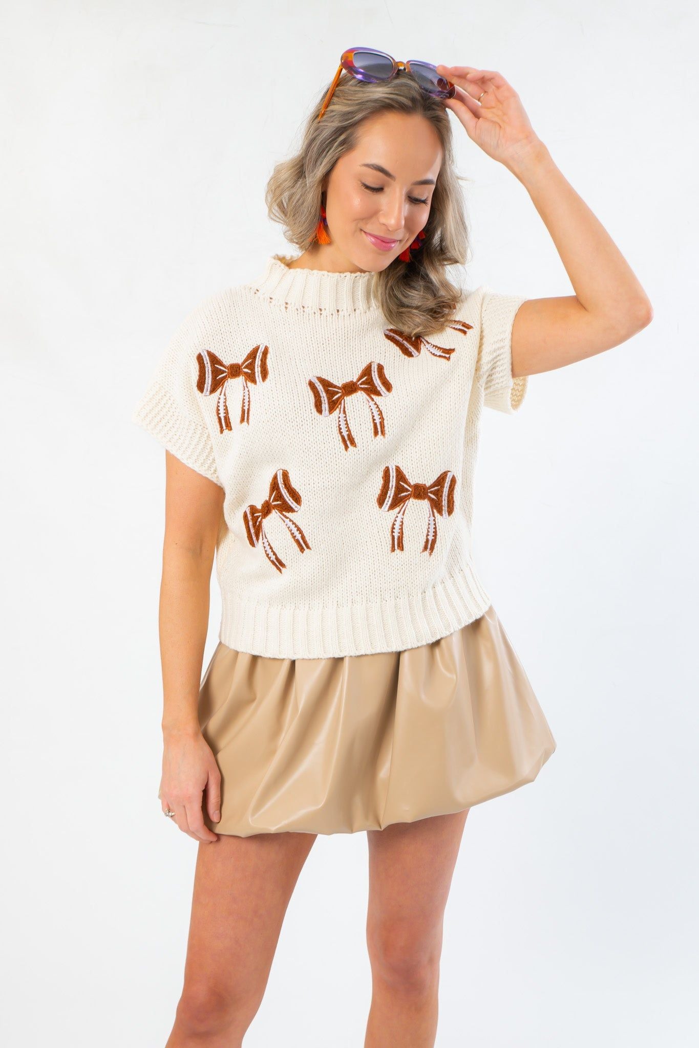 Model wearing Football Bow Mock Neck Cream Sweater with brown bow accents and short sleeves, styled for a cute and sporty gameday look.